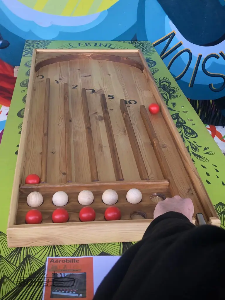 Une boule rouge sort de la piste de lancement du billard aérobille, frappée par la queue.