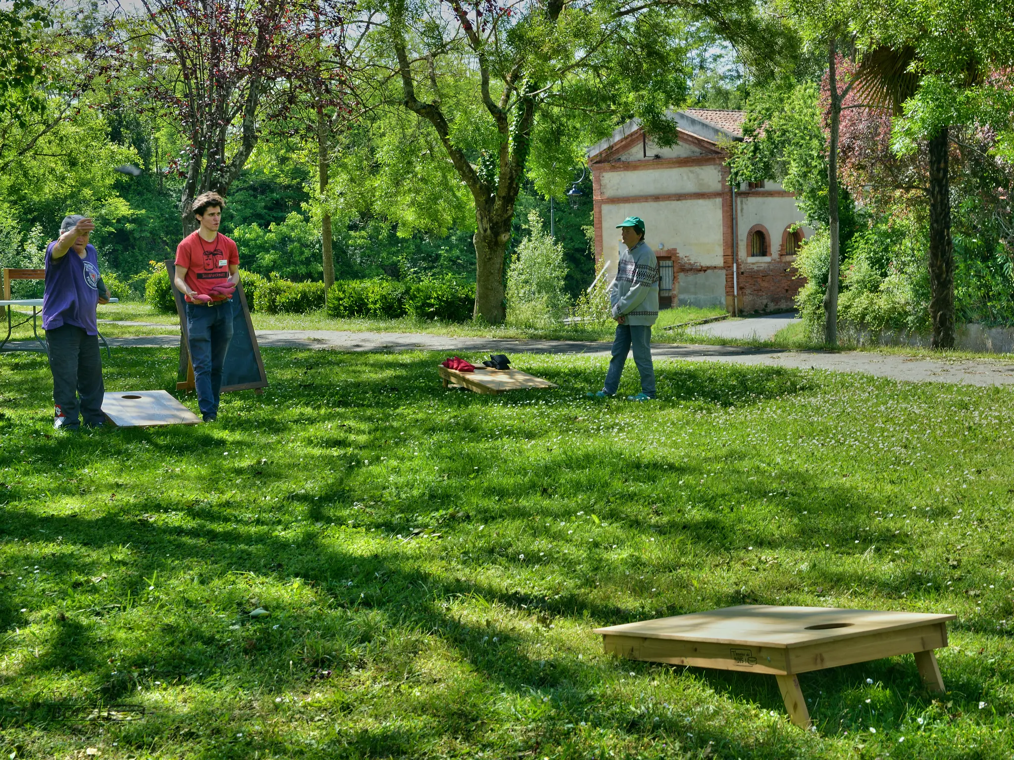 Lors d'une belle après-midi ensoleillée à Montesquieu-Volvestre en 2025. Plusieurs personnes jouent au cornhole, dont votre serviteur : Alexandre Sahuguède.