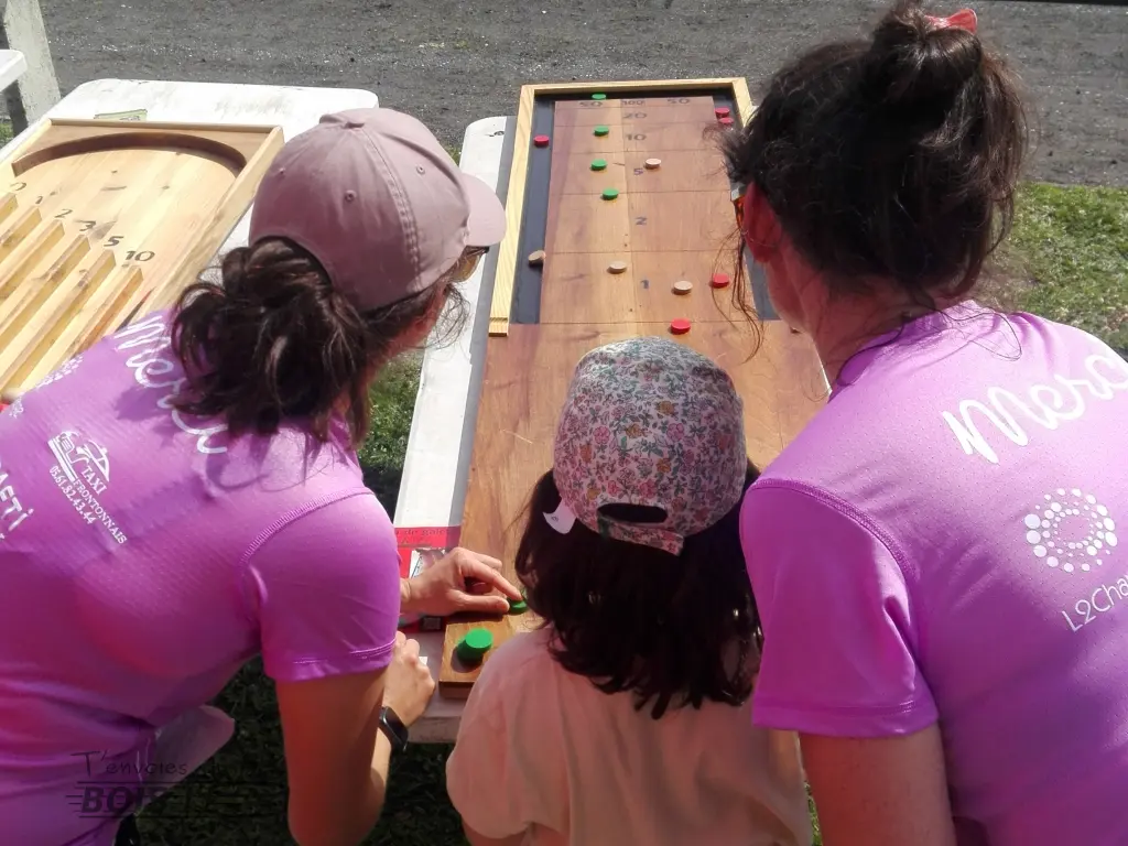 Deux femmes et une enfant jouent ensemble au jeu de galets. Ce jeu en bois traditionnel du XVIᵉ siècle a encore la cote ! Photo prise lors de la course Elles run pour toutes en 2025.