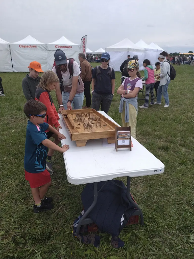 Un adulte essaie le billard labyrinthe devant un attroupement d'enfants. Photo prise lors du meeting aérien AirExpo en mai 2026.