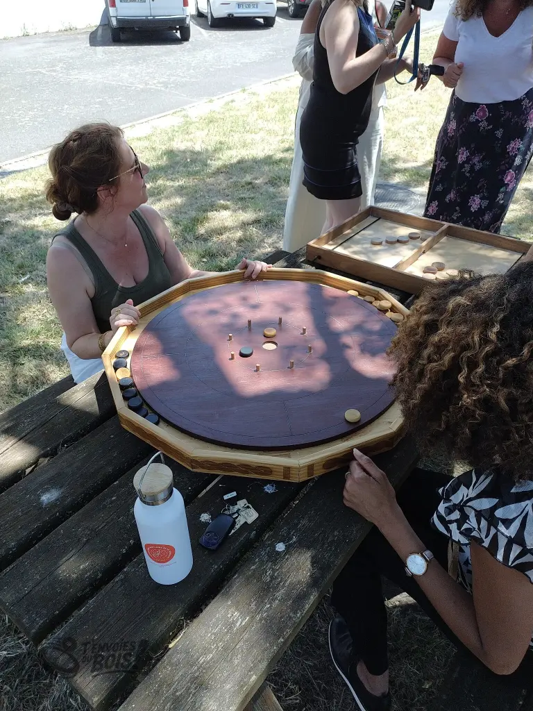 Deux femmes jouent au crokinole sur une table de pique-nique lors d'une après-midi festive à la PJJ. Photo prise en juin 2026.